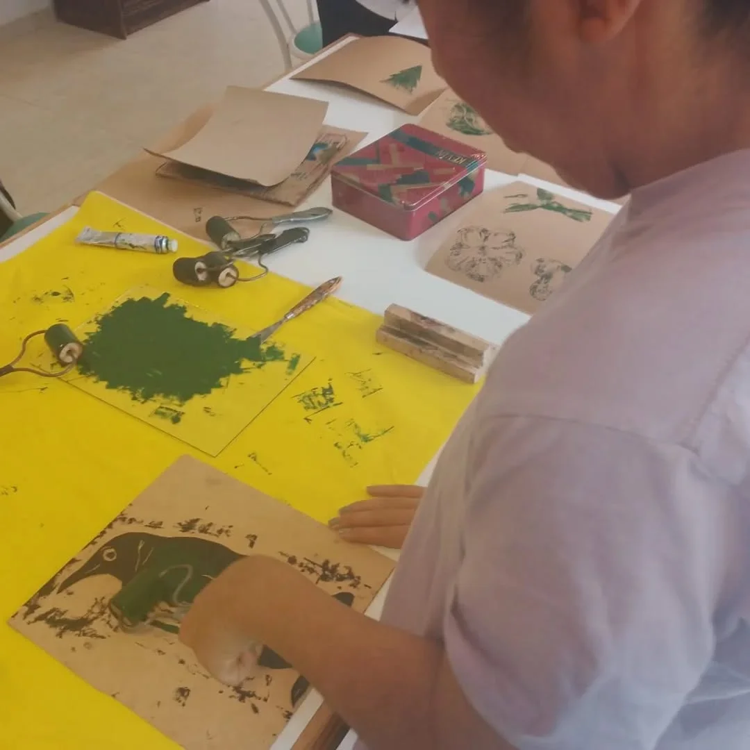 Un participante trabaja con pintura amarilla y verde sobre la mesa.