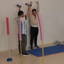 Dos personas comparten una actividad junto a postes y una colchoneta.
