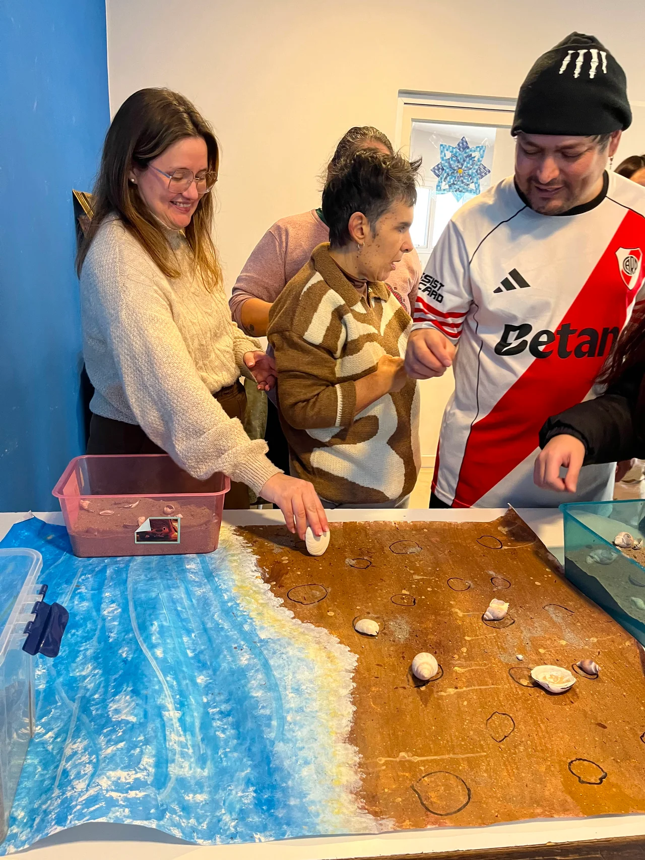 Personas exploran una mesa con materiales que representan agua y arena.
